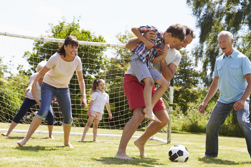 Multi Generation Playing Football In Garden Together